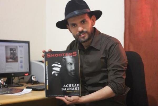 الفنان الفوتوغرافي أشرف بزناني يحمل مجلة بريطانية ظهر على غلافها 